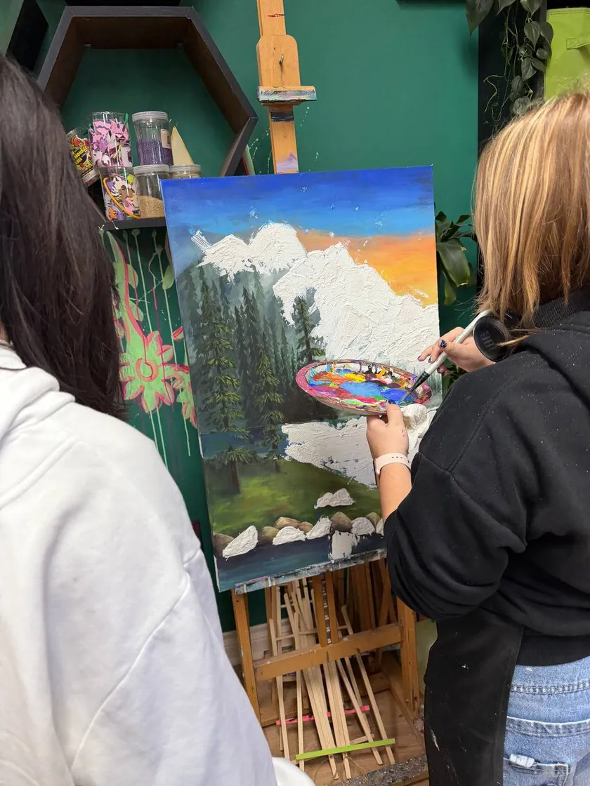 Student painting a mountain landscape at the easel with teacher guidance