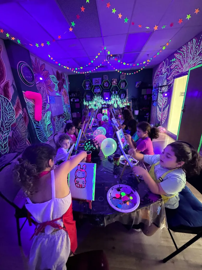 Children painting at easels in the glow-in-the-darkened art room