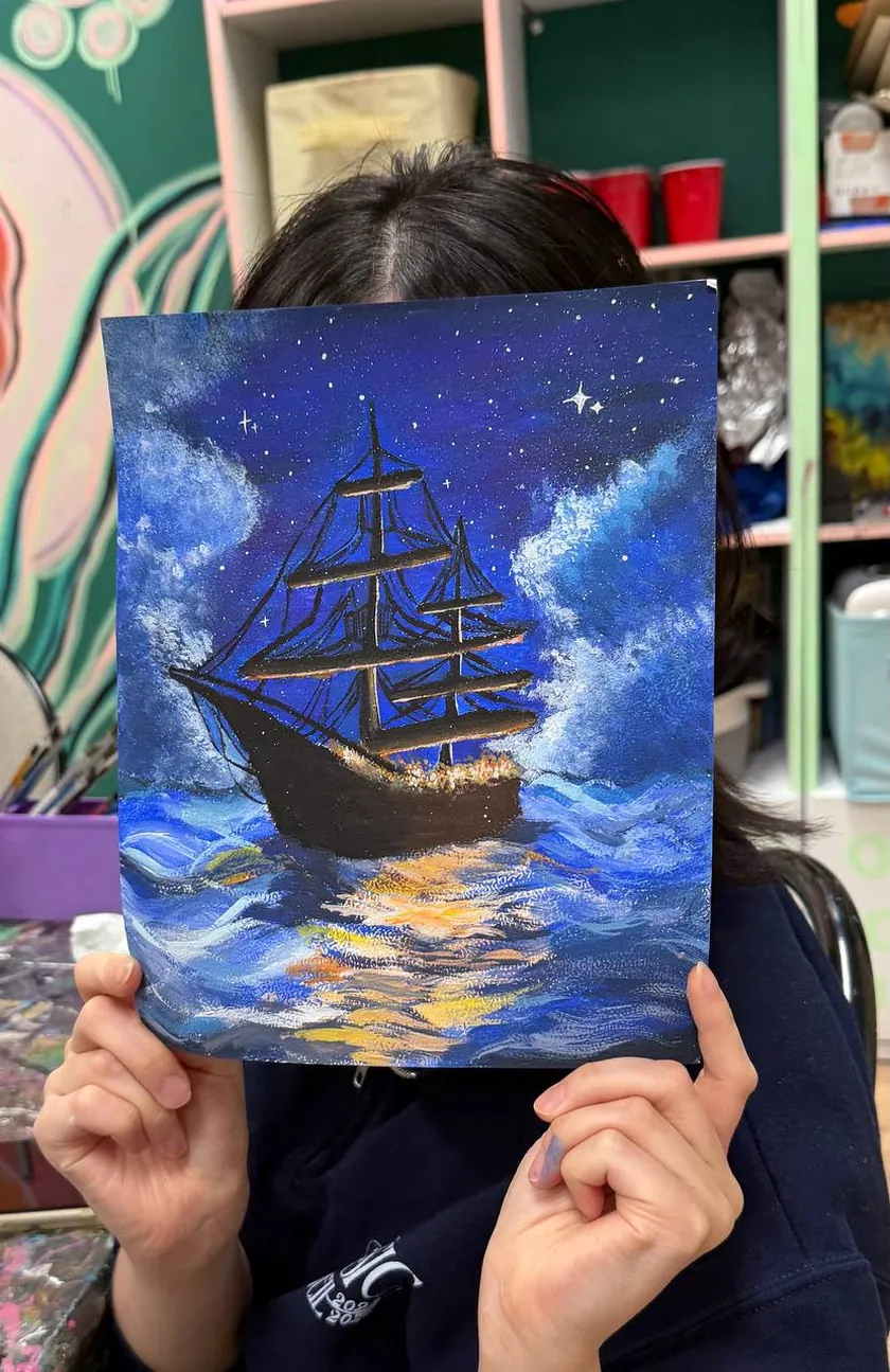 Student holding an acrylic painting of a tall ship at night