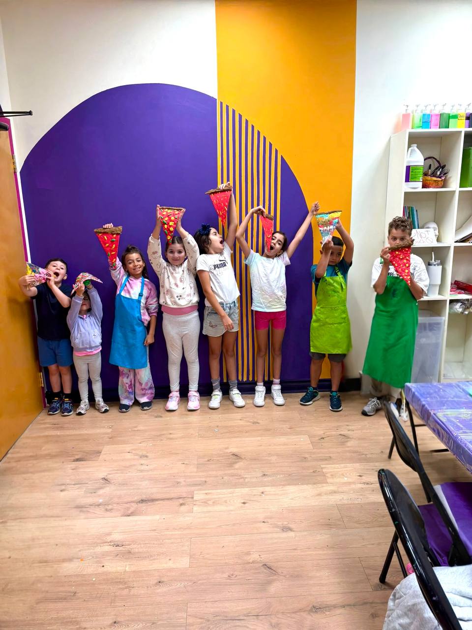Campers holding up the paper pizza slices they made in the craft workshop